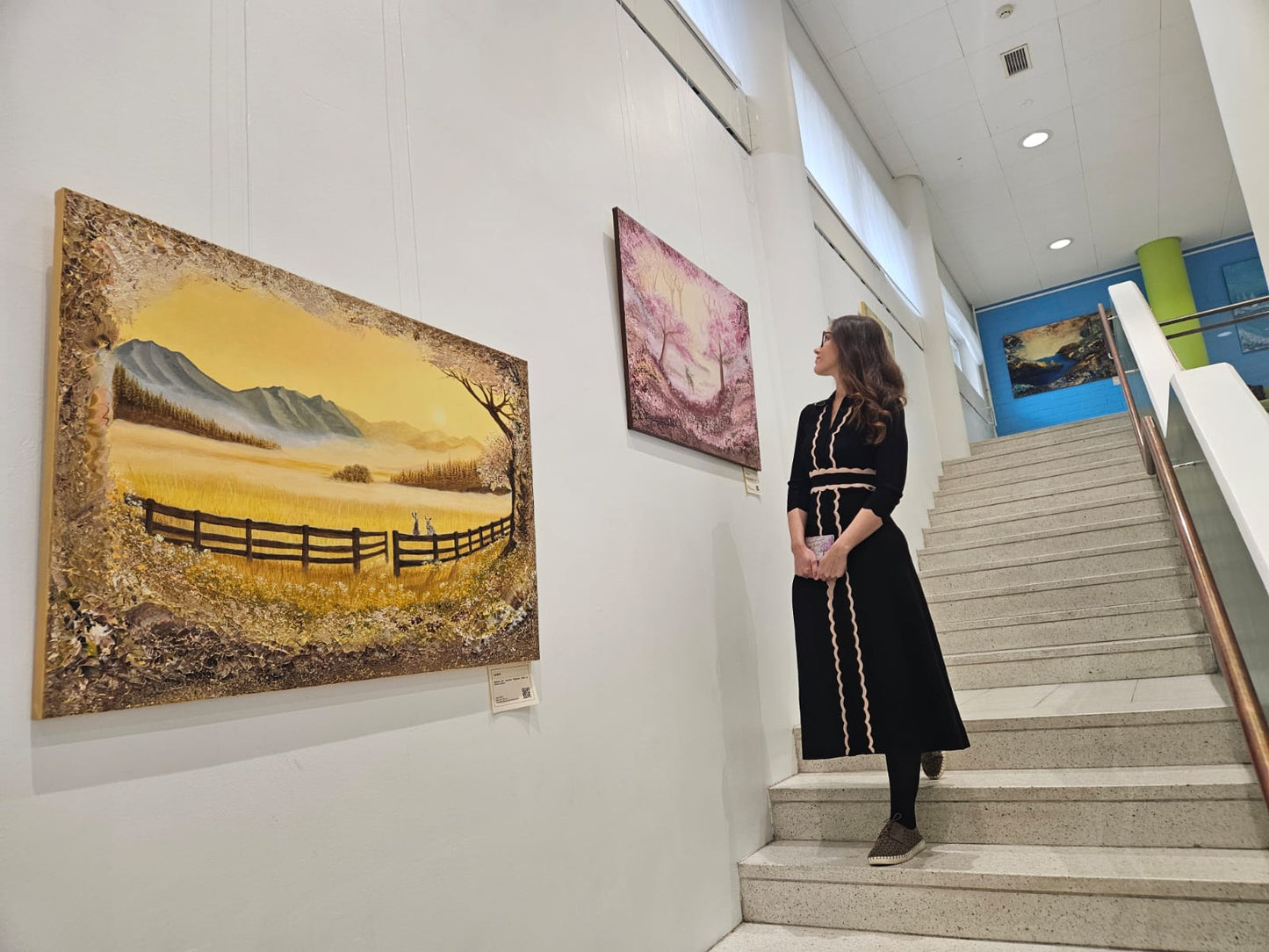 Woman standing on a staircase looking at wall art in an art gallery.